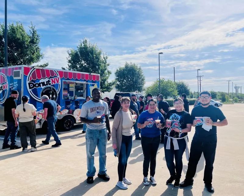 Team members with donuts and lemonade outside the shop on a sunny morning