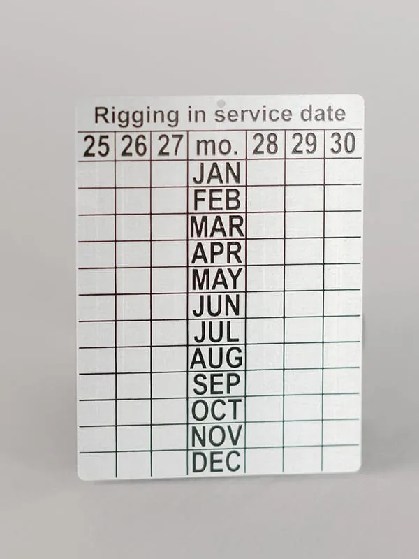 An aluminum rigging in-service date tag with punch-out month and year grid