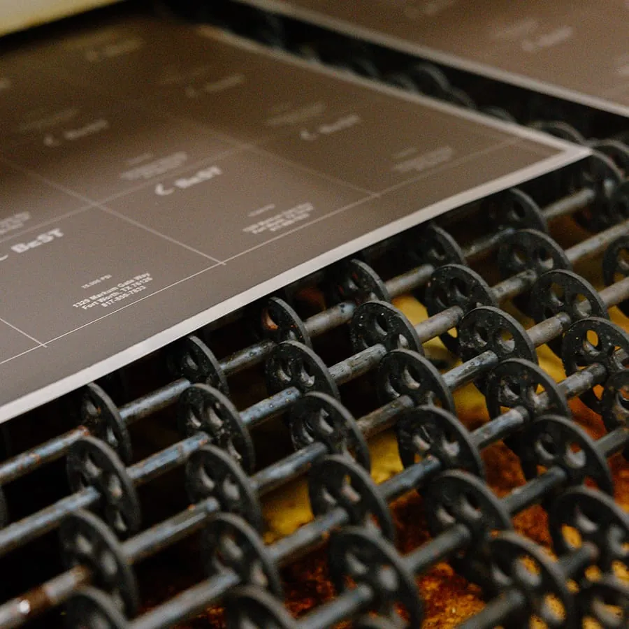 An etched nameplate sheet riding out of the etch line on its conveyor rollers