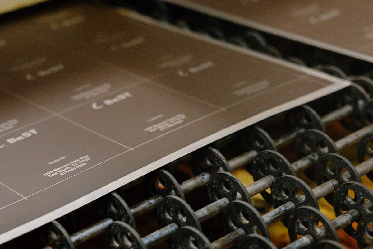 An etched nameplate sheet riding out of the etch line on its conveyor rollers