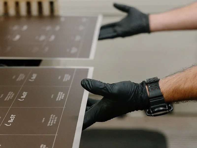 Gloved hands feeding etched sheets at the machine table