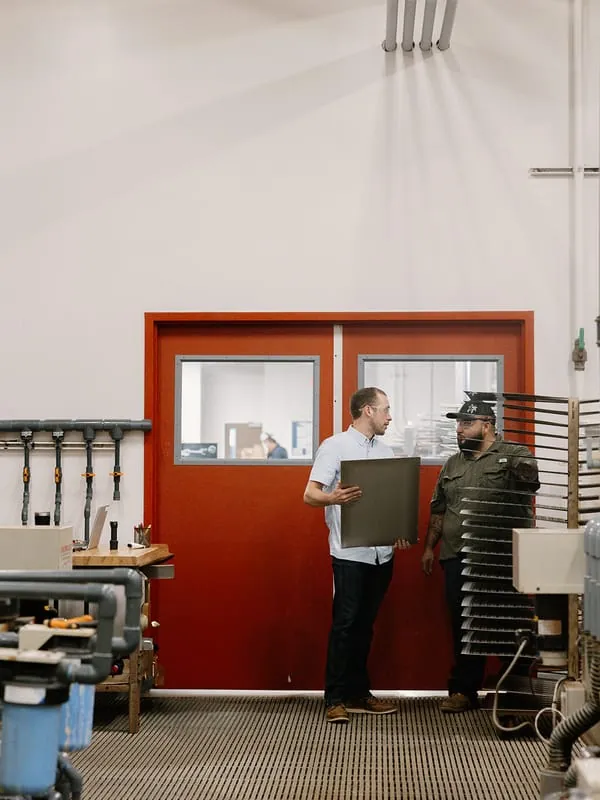 Two team members talking over a freshly etched plate at the etch room door