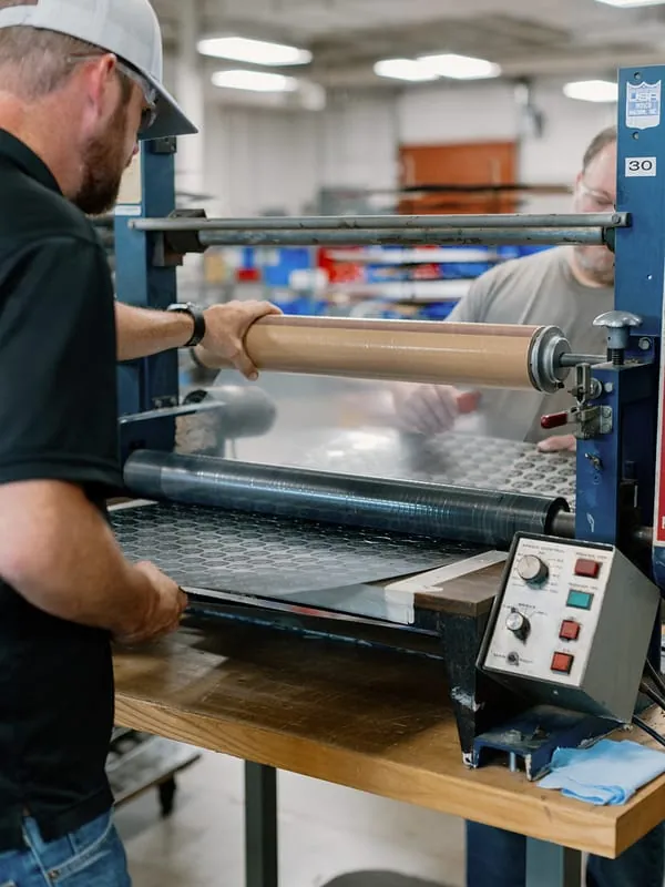 Two team members feeding a plate through the laminator rollers