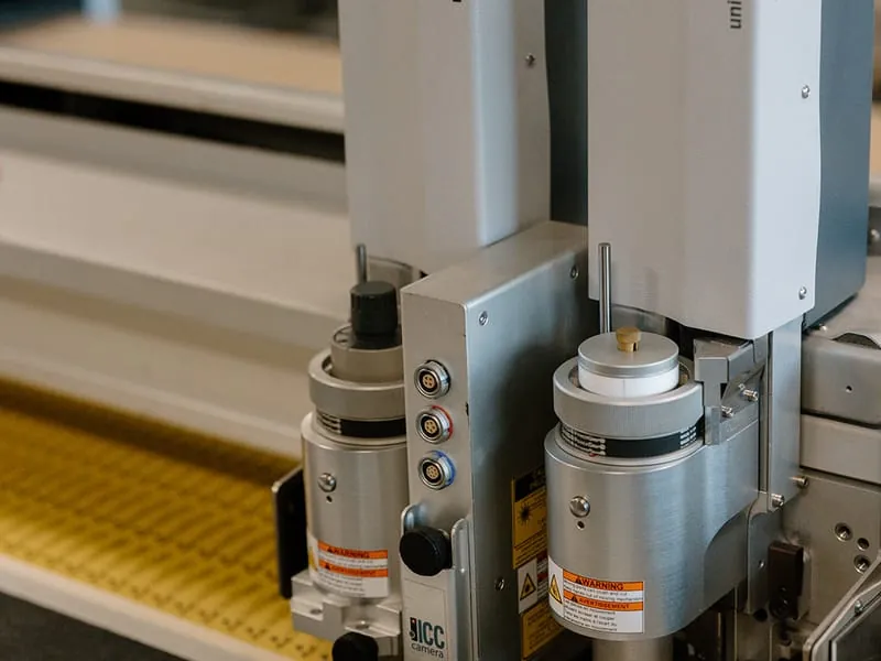 The twin cutting heads of the Zund flatbed knife cutter over a sheet of serialized tags