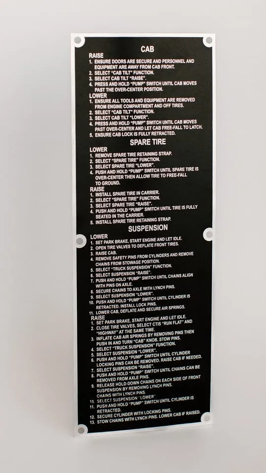 A black Metalphoto cab instruction plate with raise, lower, spare tire, and suspension procedures